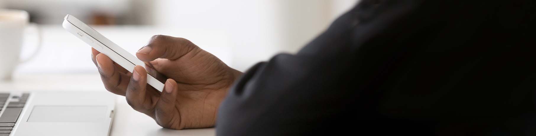 Person looking at their smartphone, sat by laptop